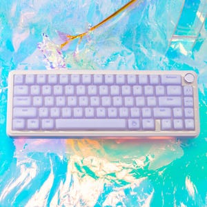 May include: A compact mechanical keyboard with a white frame and light purple keycaps. The keyboard features a standard QWERTY layout, a circular knob in the top right corner, and various function keys. The keys are backlit with a soft glow.