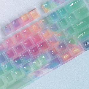 Może przedstawiać: Kolorowa osłona klawiatury z tęczowym wzorem tie-dye. Przezroczysta osłona pasuje na klawisze, z widocznymi literami i symbolami. Klawisze są oznaczone literami, cyframi i klawiszami funkcyjnymi.
