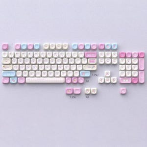 May include: A mechanical keyboard with pastel keycaps in pink, light blue, and white. The keycaps are arranged on a light purple surface. Some keys have small icons. The keyboard is disassembled.