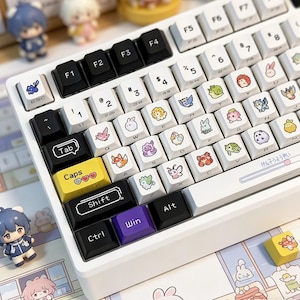Puede incluir: Teclado mecánico blanco con teclas personalizadas con diseños de animales de dibujos animados coloridos. El teclado tiene teclas de acento negras y amarillas, y pequeñas figuras están colocadas alrededor del teclado.