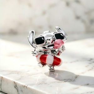 May include: A silver-toned charm featuring the character Stitch wearing black sunglasses and holding a pink ice cream cone. The character is positioned inside a red and white striped circular floatie, showcasing a polished metallic finish.