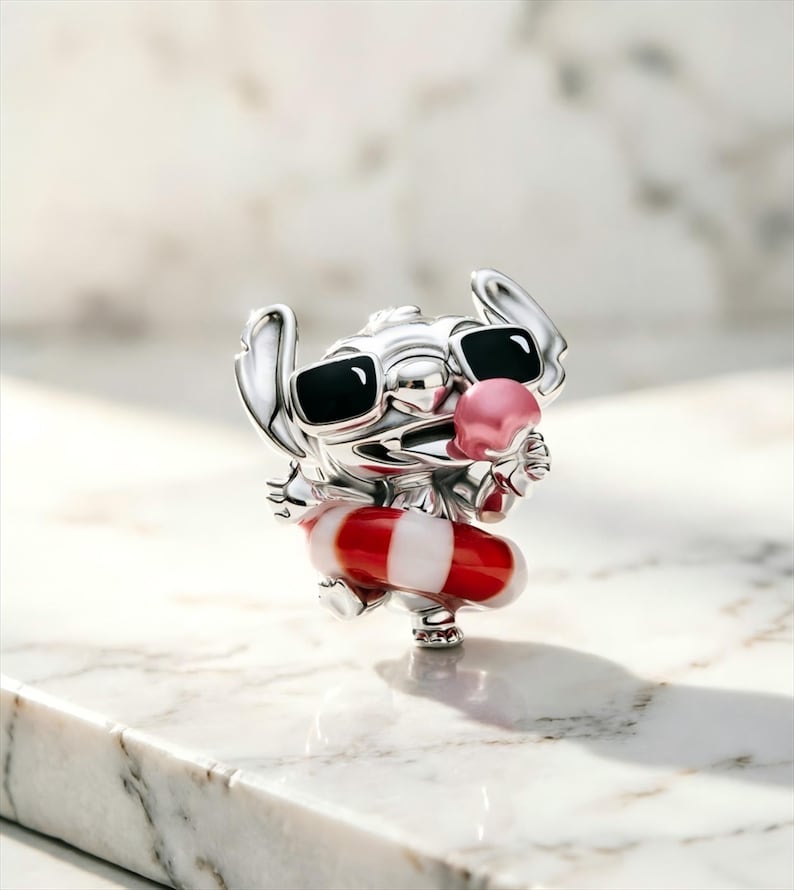 May include: A silver-toned charm featuring the character Stitch wearing black sunglasses and holding a pink ice cream cone. The character is positioned inside a red and white striped circular floatie, showcasing a polished metallic finish.