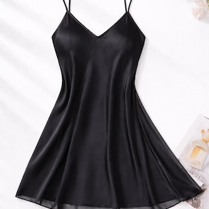 May include: A black satin slip dress with thin spaghetti straps and a V-neckline. The dress has a flowing, A-line skirt and a sheer hemline. The image is set against a white background with floral accents, suggesting a lingerie or sleepwear theme.