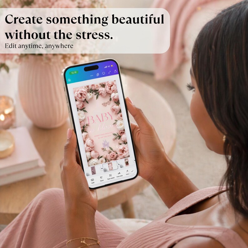 May include: A smartphone displays a baby shower invitation design with floral elements. The phone is held by a person wearing a pink top. Text at the top reads, "Create something beautiful without the stress. Edit anytime, anywhere."