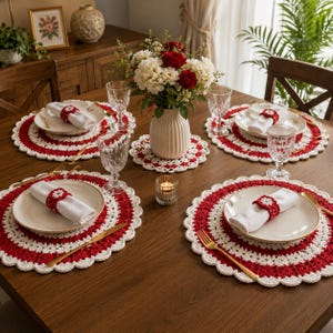 May include: A dining table setting featuring four round white and red crocheted placemats, matching crocheted napkin rings, white cloth napkins, clear glass goblets, gold-toned flatware, and a central white vase with red and white flowers.