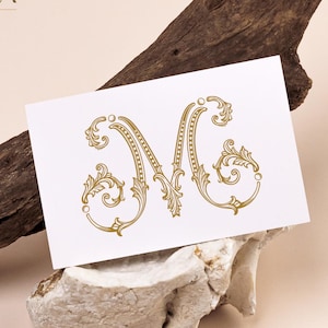 May include: A white card with a gold letter "M" in an ornate, vintage style. The card is propped on a piece of stone and a piece of wood. The text "CALISTA monogram set" is at the top.