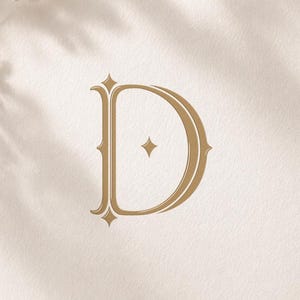 Könnte beinhalten: Ein goldfarbenes Monogramm des Buchstabens "D" mit dekorativen Verzierungen, zentriert auf einer cremefarbenen Karte. Das Wort "MONOGRAM" steht oben. Das Bild enthält einen Stift, ein Band und florale Akzente. Der Text "Monograms Logos Alwih" steht unten.