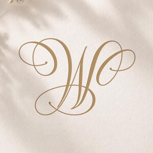 Può includere: Un monogramma color oro della lettera "W" in uno stile di scrittura decorativo è centrato su una carta color crema. La parola "MONOGRAM" è in alto. Una penna e un nastro dorati sono a destra. Delicati fiori bianchi sono a sinistra.