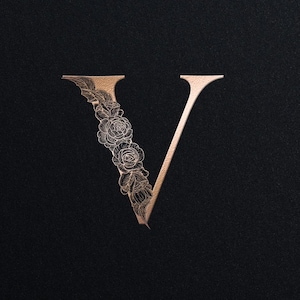 Peut inclure: Une lettre "V" dorée avec des ornements floraux, sur fond noir. Le texte "PERSONAL MONOGRAM" est en haut et "Monograms Logos Alwih" en bas. Le design est élégant et adapté à l'image de marque.