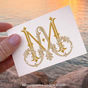 May include: A white card featuring a gold monogram design with the letters "N" and "M" intertwined. The design includes ornate flourishes and decorative elements. The card is held against a backdrop of water and a sunset. The text "Monograms Logos Alwih" is at the bottom.