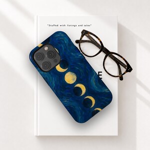Puede incluir: Una funda para smartphone con un fondo de estilo pintura al óleo texturizada en azul oscuro y una serie de fases lunares amarillas dispuestas en diagonal. Junto a la funda, unas gafas con patrón de carey sobre un libro blanco con el texto Stuffed with listings and tales.