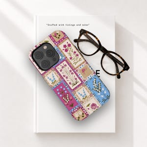 May include: A floral patterned phone case with a patchwork design in pink, blue, and beige. The case is on a white book with the text "Stuffed with listings and tales." Tortoiseshell glasses rest on the book.