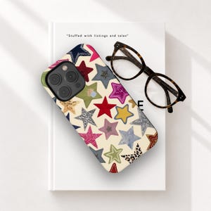 May include: A smartphone case with a cream-colored background featuring a repeating pattern of multi-colored stars in various textures and prints, including red, yellow, blue, pink, green, and leopard print, alongside a pair of dark brown eyeglasses.