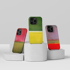 Könnte beinhalten: Drei Smartphone-Hüllen mit abstrakten Farbblock-Designs. Die linke Hülle ist rosa und olivgrün, die mittlere Hülle ist waldgrün und leuchtend gelb, und die rechte Hülle ist in gedecktem Lila, Olivgrün und leuchtendem Rot gehalten.