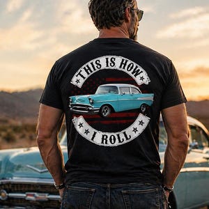 以下が含まれることがあります： 「THIS IS HOW I ROLL」の文字と水色のクラシックカーのグラフィックがプリントされた黒いTシャツ。 ヴィンテージのガソリンスタンドの看板と夕焼けを背景にした砂漠の風景。