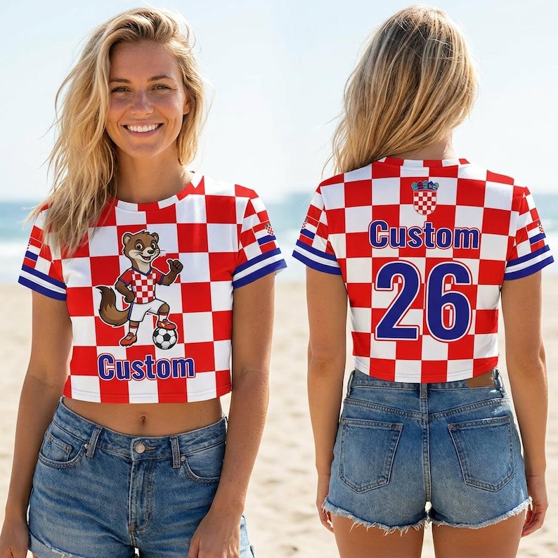 May include: A short-sleeved crop top featuring a red and white checkered pattern. The front displays a cartoon animal wearing a matching jersey with a soccer ball and the word Custom. The back shows the word Custom and the number 26 in blue.