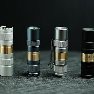 May include: Four cylindrical flashlights arranged in a row, each featuring a central brass band and knurled metal sections. The flashlights vary in color, including silver, dark gray, and black, with some models equipped with a metal pocket clip.