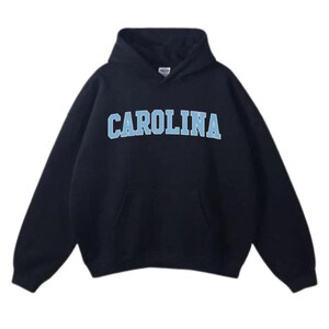 May include: A navy blue hooded sweatshirt featuring the word "CAROLINA" in light blue block letters. The sweatshirt has a front pocket and a drawstring hood. The material looks soft and comfortable, suitable for casual wear.