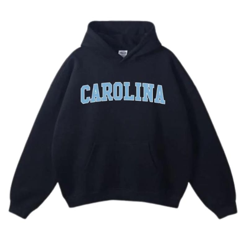 May include: A navy blue hooded sweatshirt featuring the word "CAROLINA" in light blue block letters. The sweatshirt has a front pocket and a drawstring hood. The material looks soft and comfortable, suitable for casual wear.