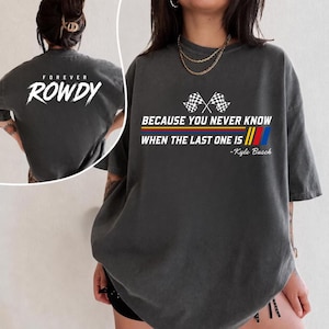 May include: Dark gray t-shirt with the text "FOREVER ROWDY" on the back and "BECAUSE YOU NEVER KNOW WHEN THE LAST ONE IS" with checkered flags and the name "Kyle Busch" on the front. The shirt has a vintage, worn look.