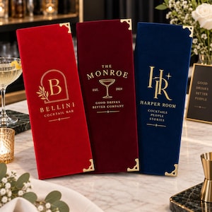 Könnte beinhalten: Drei rechteckige Menükartenhüllen aus rotem, dunkelrotem und marineblauem Samt mit goldenen Metalleckenschützern und Goldfolienprägung. Die rote Hülle zeigt Bellini Cocktail Bar, die dunkelrote The Monroe und die blaue Harper Room.