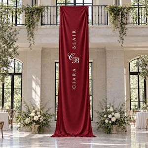 Può includere: Un lungo striscione verticale in tessuto rosso intenso appeso alla ringhiera di un balcone. Lo striscione presenta una scritta bianca che recita CIARA BLAIR con un monogramma CB stilizzato al centro. Il tessuto cade a terra in morbide pieghe.