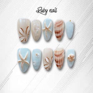 Könnte beinhalten: Ein Set aus zehn künstlichen Nägeln mit Strandmotiv. Die Nägel zeigen Designs von Muscheln, Seesternen und floralen Mustern in Beige, Braun und Hellblau. Der Text "Ruby nail" ist oben in Schreibschrift geschrieben.