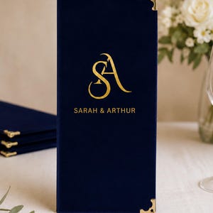 K&ouml;nnte beinhalten: Ein rechteckiger Men&uuml;einband aus marineblauem Samt mit goldenen Metalleckensch&uuml;tzern. Die Vorderseite ist mit einem goldenen Folienmonogramm der Buchstaben SA und dem darunter zentrierten Text SARAH & ARTHUR in einer serifenlosen Schrift versehen.