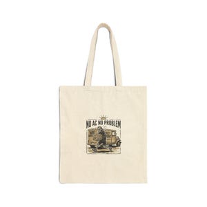 May include: Cream-coloured tote bag featuring the text "NO AC NO PROBLEM" above an illustration of a skeleton pushing a vintage truck. The bag has a rectangular shape and two long handles.