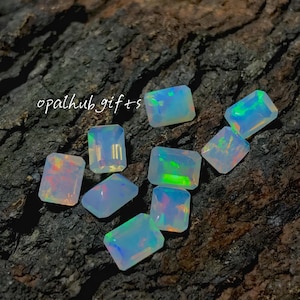 Puede incluir: Un conjunto de gemas de ópalo rectangulares con colores iridiscentes, incluyendo azul, verde y naranja. Las gemas están dispuestas sobre una superficie oscura y texturizada. El texto "opalhub gifts" es visible.