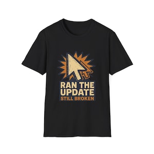 May include: Black t-shirt featuring a distressed graphic of a computer cursor and the text "RAN THE UPDATE STILL BROKEN". The design includes a beige cursor and orange burst on a navy blue background.