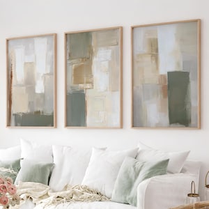 Può includere: Un set di tre quadri rettangolari con blocchi geometrici astratti in tonalità verde salvia, beige, crema e bianco. Ogni pezzo è racchiuso in una cornice di legno chiaro e presenta texture di vernice stratificate e composizioni verticali.