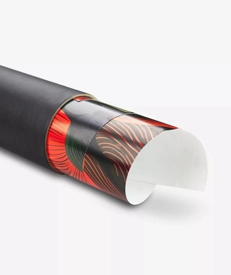 Puede incluir: Un tubo de almacenamiento cil&iacute;ndrico negro que contiene un p&oacute;ster enrollado. La parte visible del p&oacute;ster presenta un dise&ntilde;o gr&aacute;fico con l&iacute;neas curvas audaces en rojo, verde oscuro y negro, con un borde de papel blanco que se curva.