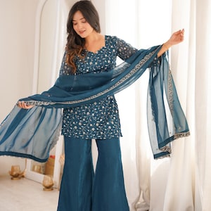 Puede incluir: Conjunto de pantalón palazzo bordado en color turquesa. El conjunto incluye una blusa de manga larga con bordado floral y pantalones de pernera ancha. Una bufanda transparente a juego con un borde decorativo completa el conjunto. Ideal para ocasiones especiales.