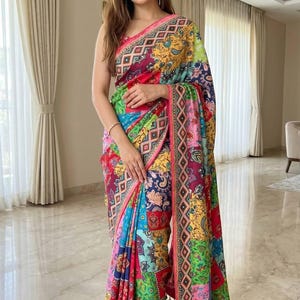 May include: A vibrant, patterned saree in shades of red, blue, green, and yellow. The fabric features a patchwork design with geometric and floral motifs. The saree has a pink border and is worn by a person.