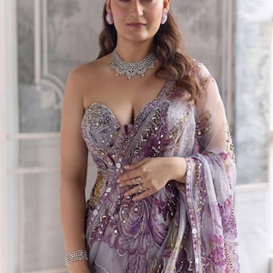 May include: A formal lavender saree with intricate floral embroidery and sequin embellishments. The saree features a strapless, embellished bodice and is paired with a matching necklace, earrings, and bracelets. The overall look is elegant and sophisticated.