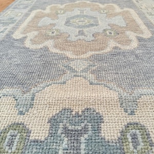 May include: A rectangular runner rug featuring a repeating floral medallion pattern in soft shades of light blue, beige, cream, and muted sage green. The woven textile has a textured, knotted pile surface with a geometric border design.