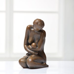 Puede incluir: Una escultura de bronce de una madre sosteniendo a un bebé en sus brazos. La madre está sentada y mirando al bebé. La escultura es una representación del amor y la maternidad.