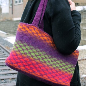 Puede incluir: Una bolsa de mano de punto a rayas de color morado, verde, naranja y rojo con un asa morada.