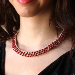 Può includere: Una collana di perline con file alternate di perline rosse e trasparenti. La collana è indossata attorno al collo e si abbina a un top nero. Le perline sono piccole e uniformemente distanziate, creando un aspetto delicato ed elegante.