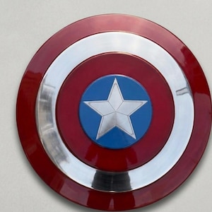 May include: A circular shield featuring a red outer ring, a silver band, and a blue central disc. A silver star is at the centre. The shield has a shiny, reflective surface.