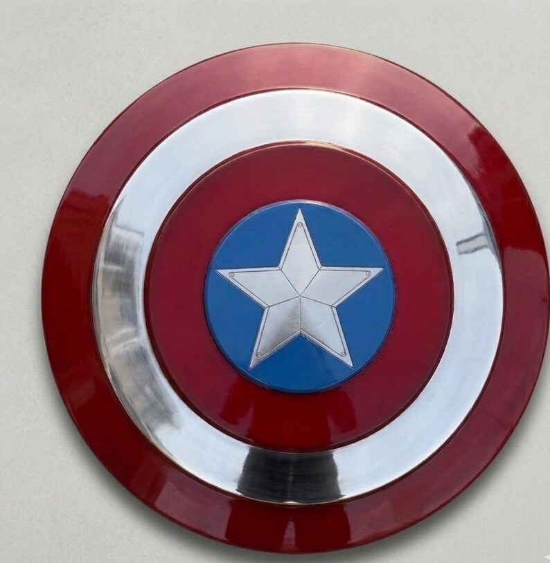 May include: A circular shield featuring a red outer ring, a silver band, and a blue central disc. A silver star is at the centre. The shield has a shiny, reflective surface.