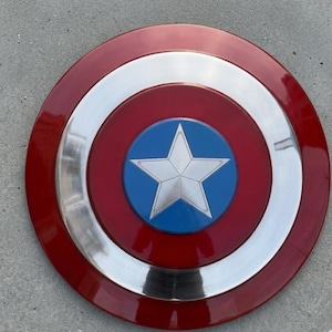 May include: A circular shield in red, white, and blue. The design includes a silver star on a blue circle at the centre, encircled by rings of red, silver, and red. This shield is a replica.