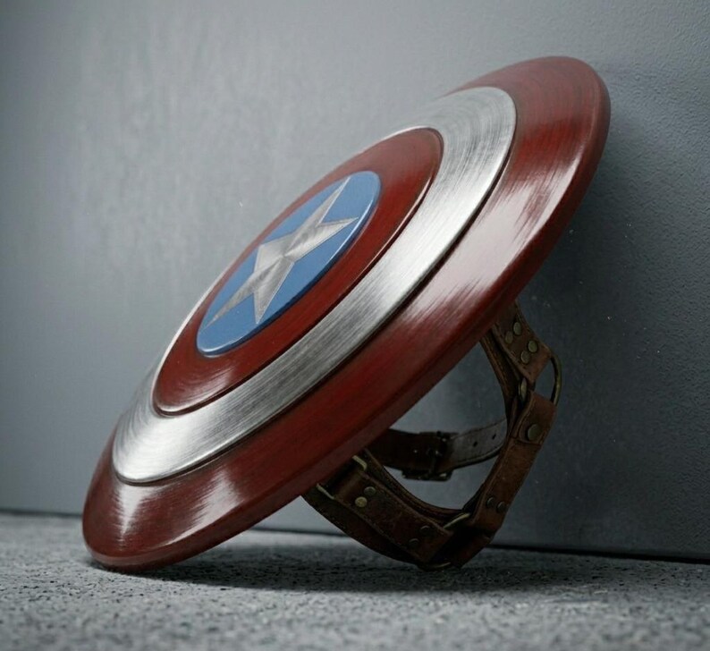 May include: A red, white, and blue shield with a star emblem, a classic superhero accessory. The shield features a metallic silver ring and brown leather straps on the back.