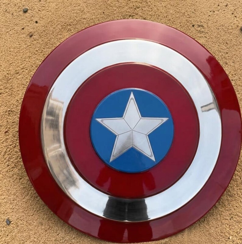 May include: A circular shield featuring a red outer ring, a silver band, and a blue central disc with a white star. The shield has a shiny surface and is likely a replica.