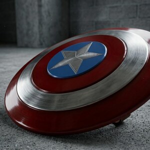 May include: A shield in red, white, and blue, featuring a star emblem. The circular design has a silver metallic ring and a blue central circle. The star is silver. The shield rests on a grey surface.