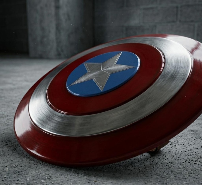 May include: A shield in red, white, and blue, featuring a star emblem. The circular design has a silver metallic ring and a blue central circle. The star is silver. The shield rests on a grey surface.