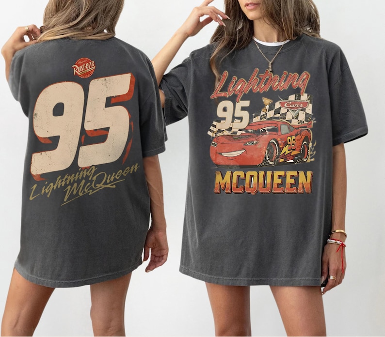 May include: A charcoal gray t-shirt featuring a graphic of the red race car Lightning McQueen with the number 95, a checkered flag, and the text Lightning McQueen. The back of the shirt displays a large number 95 and the Rust-eze logo.
