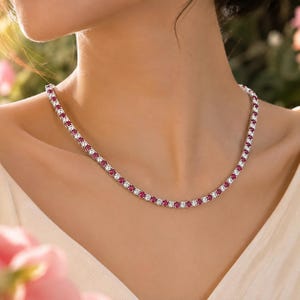 May include: A tennis necklace featuring a continuous row of alternating round-cut vibrant red rubies and clear white diamonds set in a polished metal chain that rests gracefully around the neck, showcasing a classic and symmetrical design.