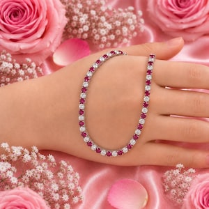 May include: A tennis bracelet featuring a continuous row of alternating round-cut vibrant red rubies and clear white diamonds set in a polished silver-toned metal band, creating a classic and elegant circular design worn around the wrist.